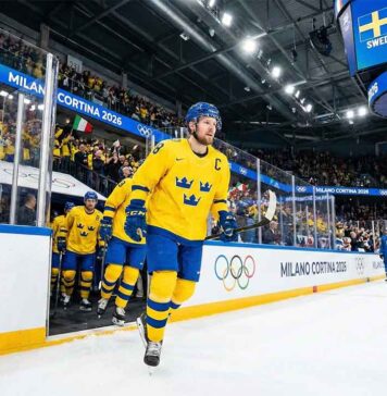Team Sweden captain Gabriel Landeskog, wearing the yellow Tre Kronor jersey with the 'C', skates out of the tunnel leading his teammates onto the ice for the Milano Cortina 2026 Winter Olympics group stage game against Team Italy.