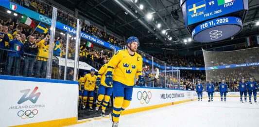 Team Sweden captain Gabriel Landeskog, wearing the yellow Tre Kronor jersey with the 'C', skates out of the tunnel leading his teammates onto the ice for the Milano Cortina 2026 Winter Olympics group stage game against Team Italy.