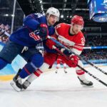 Auston Matthews (USA) and Nikolaj Ehlers (Denmark) battle intensely for the puck along the boards with Olympic branding visible during the Milano Cortina 2026 Men's Ice Hockey tournament.