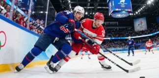 Auston Matthews (USA) and Nikolaj Ehlers (Denmark) battle intensely for the puck along the boards with Olympic branding visible during the Milano Cortina 2026 Men's Ice Hockey tournament.