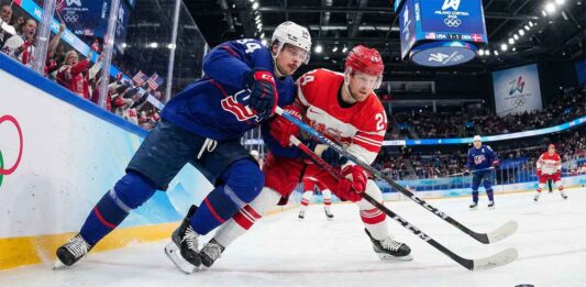 Will Team USA Crush Team Denmark? How to Watch the Epic Clash! Auston Matthews (USA) and Nikolaj Ehlers (Denmark) battle intensely for the puck along the boards with Olympic branding visible during the Milano Cortina 2026 Men's Ice Hockey tournament.