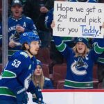 Vancouver Canucks player Teddy Blueger (53) skates past the glass where a female fan is cheering and holding up a handwritten sign that reads "Hope we get a 2nd round pick for you Teddy!".