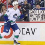 Tyler Myers Asked to Waive NMC: Are the Canucks Making a Blockbuster Trade? Vancouver Canucks defenseman Tyler Myers, wearing number 57, skates along the arena boards past a fan holding up a large handwritten sign that reads, "GOOD LUCK ON YOUR NEW TEAM TYLER!"