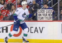 Vancouver Canucks defenseman Tyler Myers, wearing number 57, skates along the arena boards past a fan holding up a large handwritten sign that reads, "GOOD LUCK ON YOUR NEW TEAM TYLER!"