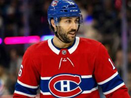 Montreal Canadiens center Vincent Trocheck, wearing his red No. 16 home jersey and a blue helmet with a visor, looks towards the right side of the rink. The background shows blurred spectators and distinct magenta and blue arena lights.