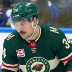 A close-up of Toronto Maple Leafs captain Auston Matthews (#34) in a Minnesota Wild jersey on the ice, appearing focused. Matthews is central to recent blockbuster NHL trade rumors linking him to the Wild.