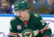 A close-up of Toronto Maple Leafs captain Auston Matthews (#34) in a Minnesota Wild jersey on the ice, appearing focused. Matthews is central to recent blockbuster NHL trade rumors linking him to the Wild.