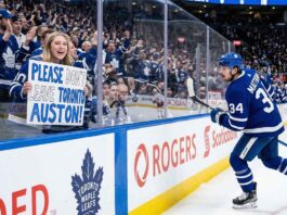 Toronto Maple Leafs fan behind glass at a hockey game holding a hand-drawn sign that says 'PLEASE DON'T LEAVE TORONTO AUSTON!' directed at Auston Matthews (#34) who is skating past on the ice.