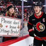 Ottawa Senators captain Brady Tkachuk skating past an emotional fan holding a handwritten sign that reads, "Please don't leave Ottawa Brady!" amid NHL trade rumors.