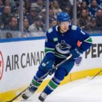 A photo of Vancouver Canucks forward Brock Boeser (#6) controlling the puck with his stick while skating along the boards during an NHL hockey game, looking up-ice.
