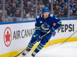 A photo of Vancouver Canucks forward Brock Boeser (#6) controlling the puck with his stick while skating along the boards during an NHL hockey game, looking up-ice.