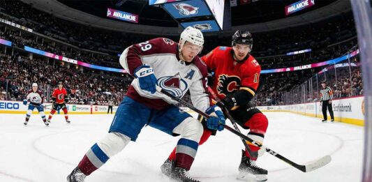 What Channel is the Calgary Flames vs Colorado Avalanche Game On Tonight? | TV & Stream Guide An action photograph capturing Colorado Avalanche forward Nathan MacKinnon and Calgary Flames forward Mikael Backlund in an intense stick battle for the puck on the ice at Ball Arena in Denver during a regular season NHL game.
