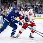 Action shot of Auston Matthews #34 (Toronto Maple Leafs) and Sebastian Aho #20 (Carolina Hurricanes) engaged in a close battle for puck possession on the ice during an NHL game.