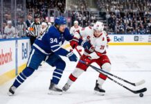 Action shot of Auston Matthews #34 (Toronto Maple Leafs) and Sebastian Aho #20 (Carolina Hurricanes) engaged in a close battle for puck possession on the ice during an NHL game.