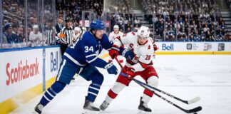 Action shot of Auston Matthews #34 (Toronto Maple Leafs) and Sebastian Aho #20 (Carolina Hurricanes) engaged in a close battle for puck possession on the ice during an NHL game.