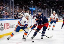 Mathew Barzal (#13) of the New York Islanders and Zach Werenski (#8) of the Columbus Blue Jackets competing for a puck during an NHL game at UBS Arena.