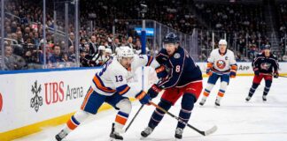 Mathew Barzal (#13) of the New York Islanders and Zach Werenski (#8) of the Columbus Blue Jackets competing for a puck during an NHL game at UBS Arena.