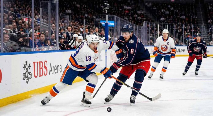 Mathew Barzal (#13) of the New York Islanders and Zach Werenski (#8) of the Columbus Blue Jackets competing for a puck during an NHL game at UBS Arena.