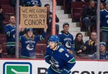 Conor Garland skates past a Vancouver Canucks fan holding a farewell sign amidst intensifying NHL trade rumors linking him to the Boston Bruins and New York Islanders.