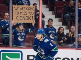 Conor Garland skates past a Vancouver Canucks fan holding a farewell sign amidst intensifying NHL trade rumors linking him to the Boston Bruins and New York Islanders.
