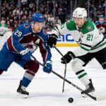 Action shot of Colorado Avalanche alternate captain Nathan MacKinnon (29) battling Dallas Stars forward Jason Robertson (21) for a loose puck during an NHL game at Ball Arena.