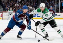 Action shot of Colorado Avalanche alternate captain Nathan MacKinnon (29) battling Dallas Stars forward Jason Robertson (21) for a loose puck during an NHL game at Ball Arena.