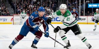 Action shot of Colorado Avalanche alternate captain Nathan MacKinnon (29) battling Dallas Stars forward Jason Robertson (21) for a loose puck during an NHL game at Ball Arena.