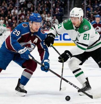 Action shot of Colorado Avalanche alternate captain Nathan MacKinnon (29) battling Dallas Stars forward Jason Robertson (21) for a loose puck during an NHL game at Ball Arena.