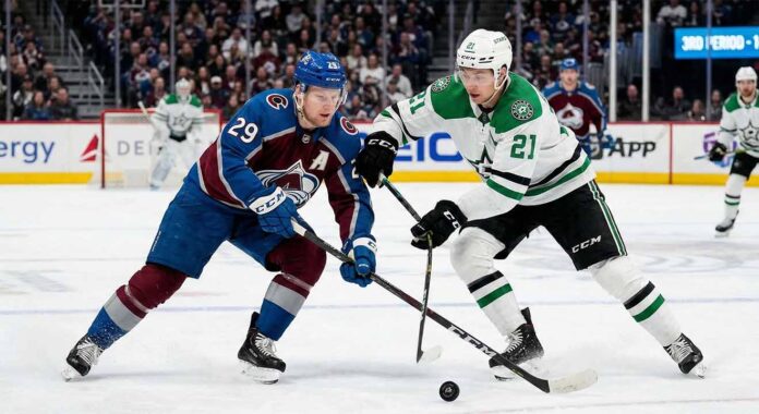 Action shot of Colorado Avalanche alternate captain Nathan MacKinnon (29) battling Dallas Stars forward Jason Robertson (21) for a loose puck during an NHL game at Ball Arena.