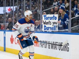 Edmonton Oilers defenseman Darnell Nurse #25 skating past a fan holding a trade sign, as rumors heat up about his $9.25M contract.