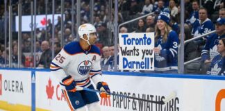 Edmonton Oilers defenseman Darnell Nurse #25 skating past a fan holding a trade sign, as rumors heat up about his $9.25M contract.