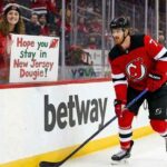 Dougie Hamilton of the New Jersey Devils skates near the boards while a fan holds a sign reading "Hope you Stay in New Jersey Dougie!" amidst offseason trade rumors.