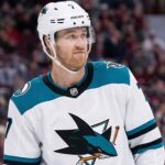 Pensive Dougie Hamilton wearing a white San Jose Sharks away uniform with teal accents, illustrating potential NHL trade rumors.
