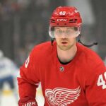 Is Elias Pettersson the Shocking Savior for the Red Wings? A concept illustration showing current Vancouver Canucks center Elias Pettersson on the ice, wearing a red Detroit Red Wings #40 home jersey and helmet, visualizing recent NHL trade rumors linking the superstar to Detroit.