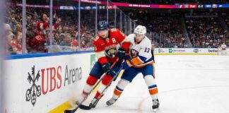 Florida Panthers forward Matthew Tkachuk (#19) and New York Islanders center Mat Barzal (#13) battling intensely for a loose puck against the boards during an NHL game at UBS Arena on March 1, 2026.