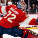Florida Panthers goaltender Sergei Bobrovsky (72) makes a dramatic full-split save against Edmonton Oilers star Connor McDavid during a high-stakes NHL game. Bobrovsky is wearing his signature red Panthers uniform and CCM goalie gear.