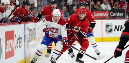 How to Watch Montreal Canadiens vs. Carolina Hurricanes: TV, Stream & Odds Montreal Canadiens captain Nick Suzuki (number 14) in white battles Carolina Hurricanes center Sebastian Aho (number 20) in red for puck control during an NHL game. The Lenovo Center logo is visible on the boards in the background.