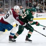 Colorado Avalanche's Nathan MacKinnon (29) checks Minnesota Wild's Quinn Hughes (43) on the boards in a fierce battle for the puck during an NHL game.