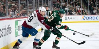 Colorado Avalanche's Nathan MacKinnon (29) checks Minnesota Wild's Quinn Hughes (43) on the boards in a fierce battle for the puck during an NHL game.