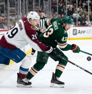 Colorado Avalanche's Nathan MacKinnon (29) checks Minnesota Wild's Quinn Hughes (43) on the boards in a fierce battle for the puck during an NHL game.