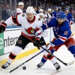 How to Watch Ottawa Senators vs New York Rangers on TV Close-up action photograph capturing Ottawa Senators' captain Brady Tkachuk (#7) and New York Rangers' center Vincent Trocheck (#16) intensely battling for the puck during an NHL game, with a blurred background of spectators and arena boards.