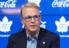 Toronto Maple Leafs Fire GM Brad Treliving – Search for Data-Centric GM MLSE President and CEO Keith Pelley speaking at a press conference about the Toronto Maple Leafs seeking a new data-centric GM. He is wearing distinctive blue-rimmed glasses and sitting in front of a blue backdrop with Maple Leafs logos and Coca-Cola branding.
