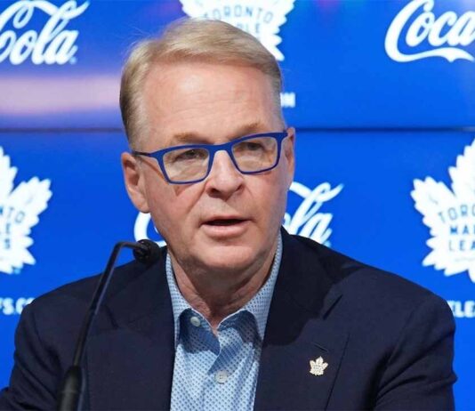 Toronto Maple Leafs Fire GM Brad Treliving – Search for Data-Centric GM MLSE President and CEO Keith Pelley speaking at a press conference about the Toronto Maple Leafs seeking a new data-centric GM. He is wearing distinctive blue-rimmed glasses and sitting in front of a blue backdrop with Maple Leafs logos and Coca-Cola branding.