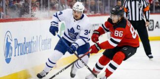 Auston Matthews (Toronto Maple Leafs captain) and Jack Hughes (New Jersey Devils) battle intensely for puck possession along the boards at Prudential Center during a game leading up to the 2026 NHL trade deadline.