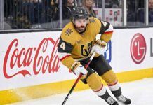 Vegas Golden Knights defenseman Rasmus Andersson, wearing the gold number 4 jersey, skates hard on the ice against the boards, illustrating the newly acquired asset facing a difficult offseason contract situation due to the NHL salary cap.