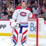 Montreal Canadiens goaltender Sam Montembeault, in full gear with his team's red, white, and blue jersey, standing by his net during an NHL game, amid swirling trade rumors and discussions about his offseason future.
