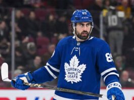 A photo of NHL player Alex Tuch wearing a blue Toronto Maple Leafs home uniform with number 89, holding a hockey stick on the ice, illustrating potential offseason free agency acquisition rumors.