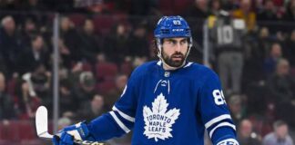 A photo of NHL player Alex Tuch wearing a blue Toronto Maple Leafs home uniform with number 89, holding a hockey stick on the ice, illustrating potential offseason free agency acquisition rumors.