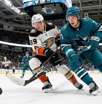 Cutter Gauthier of the Anaheim Ducks and Macklin Celebrini of the San Jose Sharks locked in a fierce battle for control of a loose hockey puck during a crucial NHL game at the SAP Center.