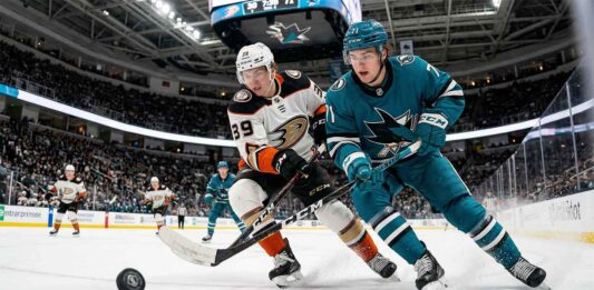 Cutter Gauthier of the Anaheim Ducks and Macklin Celebrini of the San Jose Sharks locked in a fierce battle for control of a loose hockey puck during a crucial NHL game at the SAP Center.